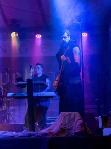Der Tod spielt im Vordergrund Bass. Weiter links etwas im Hintergrund spielt die Seelenfängerin auf dem Keyboard